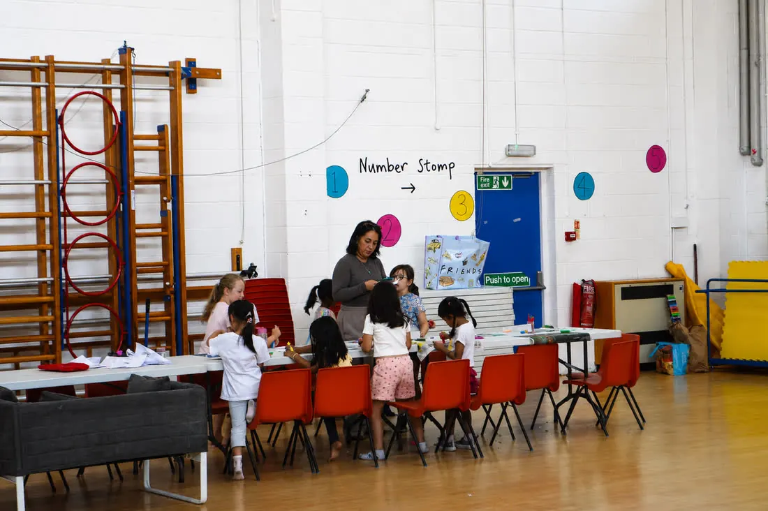 A coach helping children at the craft table in the school hall