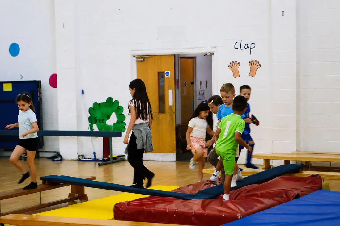 A group of children crossing the balance beams and crash mats in the hall